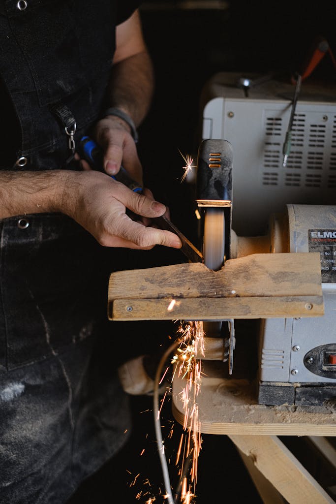 Unrecognizable male master in apron using special machine to sharpen wooden detail while working in professional joinery with special instrument